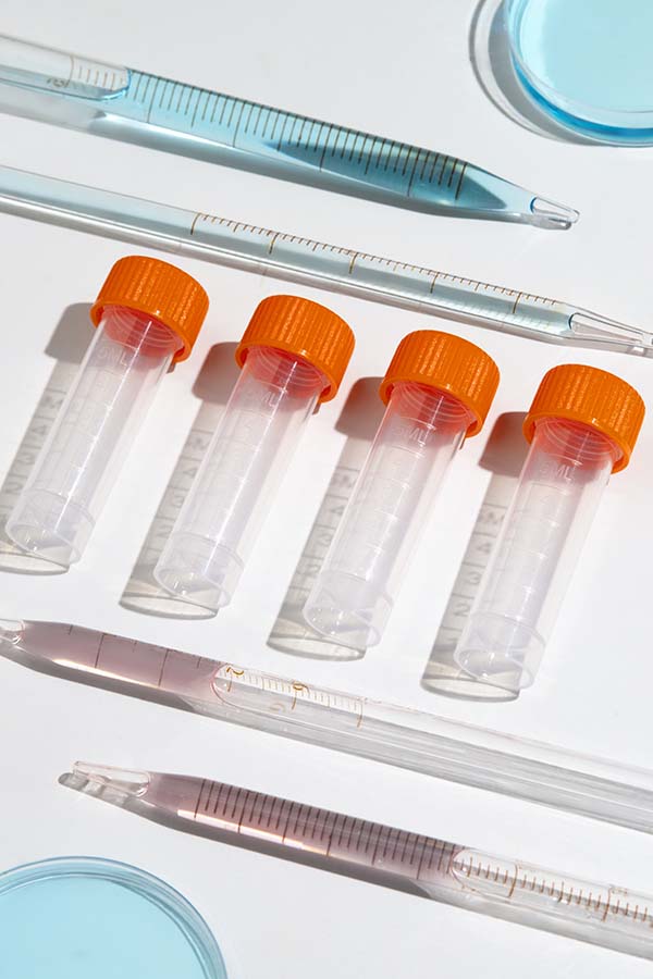 A set of empty plastic vials with orange caps, pipettes, and a petri dish arranged on a white surface, used for hormone testing.