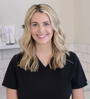 Ally, a team member at FaceTyme with Jeanine, smiles warmly with blonde hair and a black top, in front of skincare products.